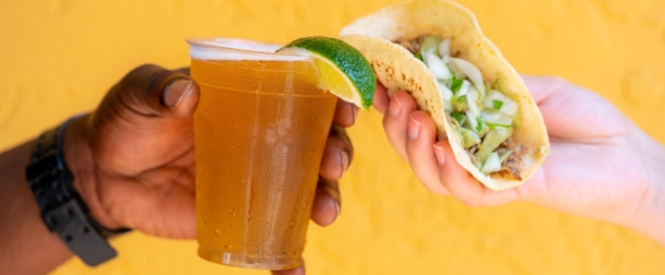One hand holding a beer, one hand holding a taco- doing a cheers motion at Red Mesa Mercado